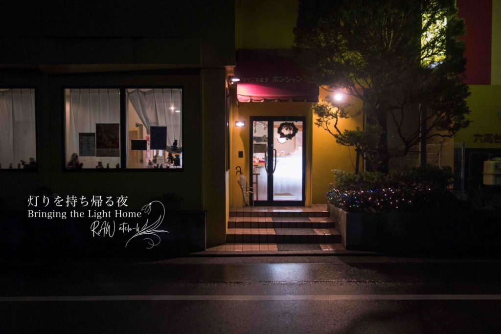 夜の街で、長男の誕生日ケーキを買った洋菓子店の入口。店内の灯りが外にこぼれ、静かな夜道に温かさを感じる風景。