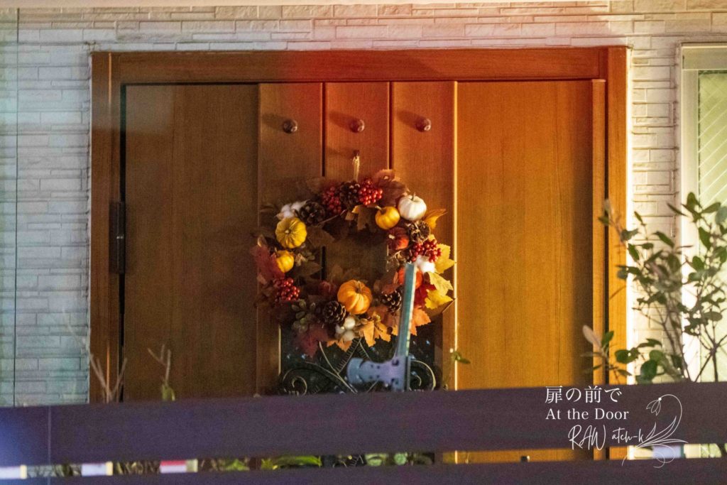 夕暮れの玄関扉に、秋色のリースが静かに掛けられている。
室内から漏れるあたたかな光が木製のドアを照らし、
誰かを迎え入れるような、穏やかな気配が漂っている。